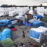 epa05095992 A migrant walks among the tents and huts of the makeshift camp called 'The Jungle' next to the fenced area made of containers recycled in rooms to host some 1,500 migrants in Calais, France, 10 January 2016. A new area of the camp will be inaugurated on 11 January as containers recycled as rooms will host its first occupants. Only half of a capacity of 1,500 places will be filled during the days. Between 4,000 and 7,000 migrants are currently living in 'The Jungle'. EPA/ETIENNE LAURENT 